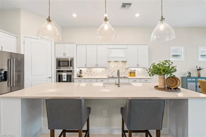 Kitchen with decorative backsplash, stainless steel appliances, white cabinetry, a large island, and recessed lighting