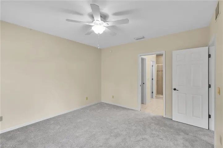 Unfurnished bedroom with light colored carpet, a ceiling fan, and connected bathroom
