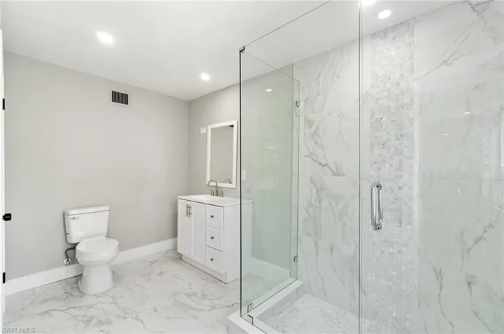 Bathroom with recessed lighting, a shower stall, marble finish floors, baseboards, and toilet