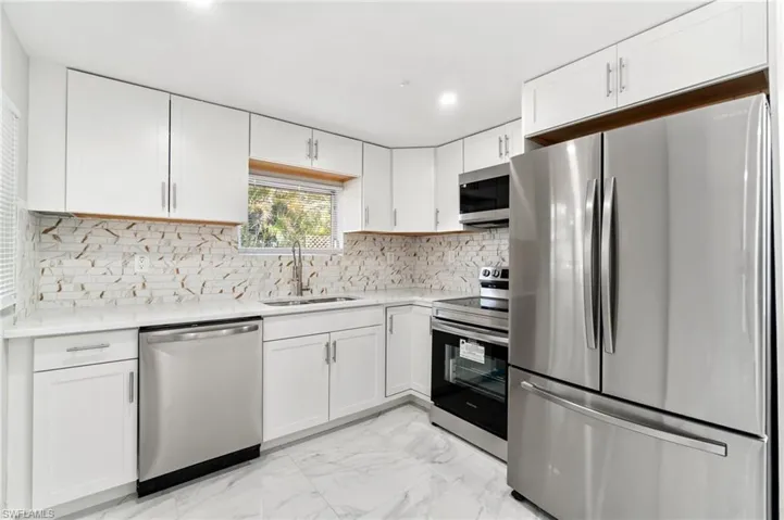 Kitchen featuring stainless steel appliances, a sink, light countertops, white cabinetry, and recessed lighting