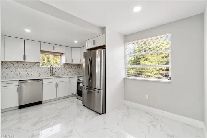 Kitchen featuring appliances with stainless steel finishes, a sink, baseboards, backsplash, and light countertops