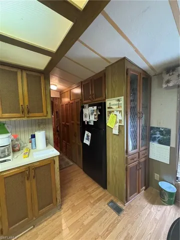 Kitchen with brown cabinetry, visible vents, freestanding refrigerator, light countertops, and light wood-style floors