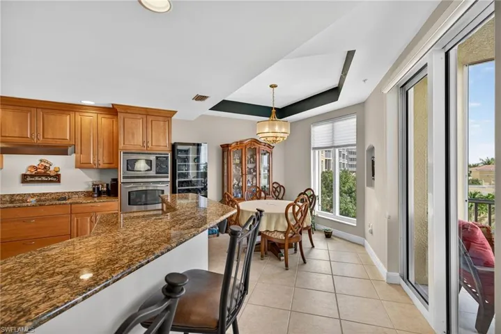 Kitchen with a breakfast bar area, dark stone countertops, a raised ceiling, brown cabinetry, and decorative light fixtures