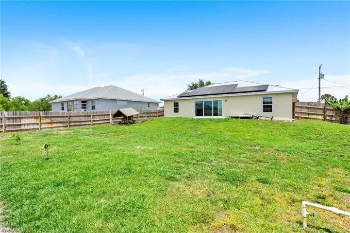 Rear view of house with roof mounted solar panels, stucco siding, and a fenced backyard