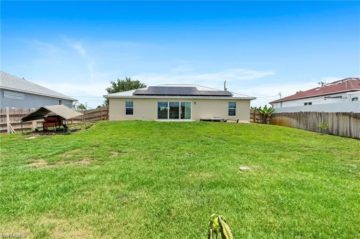 Back of house featuring stucco siding, solar panels, and a fenced backyard