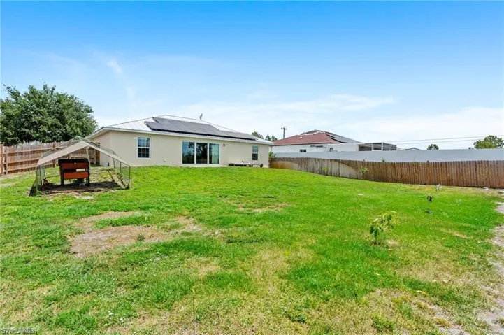 Back of house with a fenced backyard, roof mounted solar panels, and stucco siding