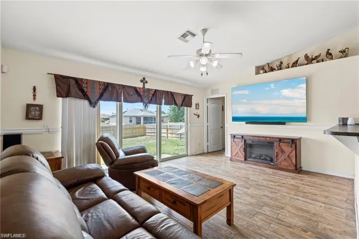 Living area featuring wood finished floors, a glass covered fireplace, a ceiling fan, and vaulted ceiling