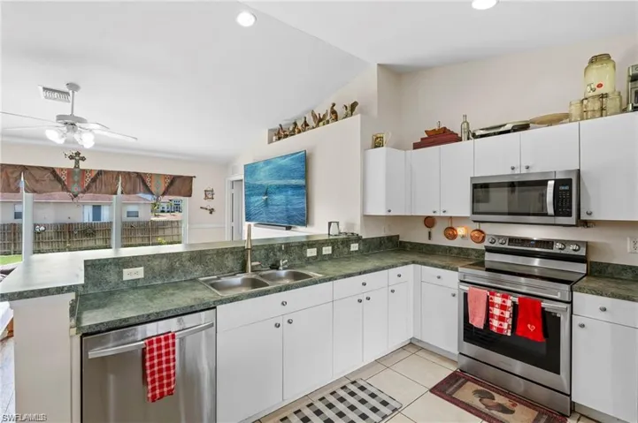 Kitchen featuring appliances with stainless steel finishes, light tile patterned floors, dark countertops, a peninsula, and white cabinets