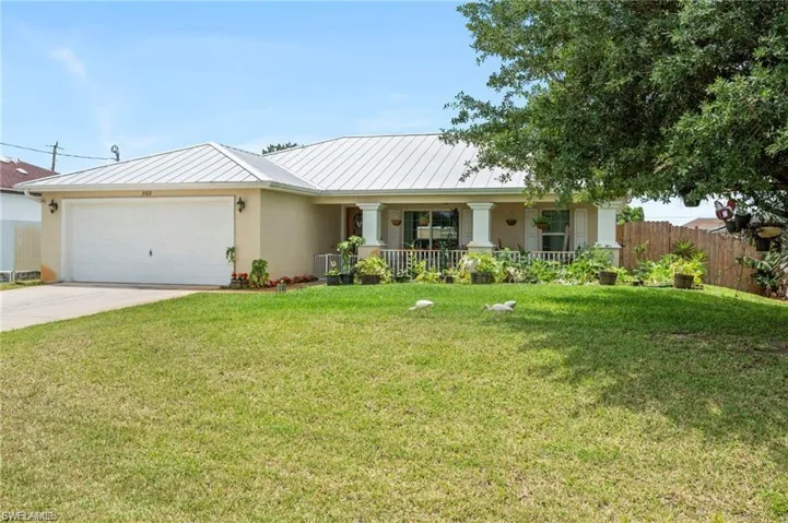 View of front of home with stucco siding, concrete driveway, an attached garage, a standing seam roof, and covered porch