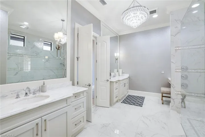 Bathroom featuring a chandelier, crown molding, two vanities, a marble finish shower, and light marble finish flooring