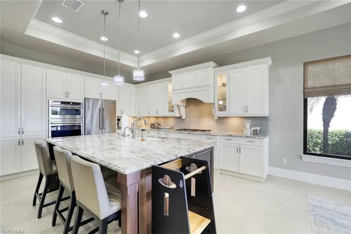 Kitchen with glass fronted cabinets, light stone counters, pendant lighting, white cabinetry, and crown molding