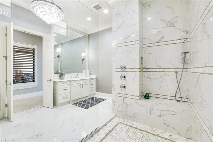 Full bathroom with crown molding, a marble finish shower, vanity, suspended lighting, and light marble finish flooring