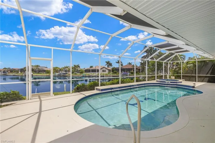 View of swimming pool featuring a patio, a water view, a pool with connected hot tub, and glass enclosure