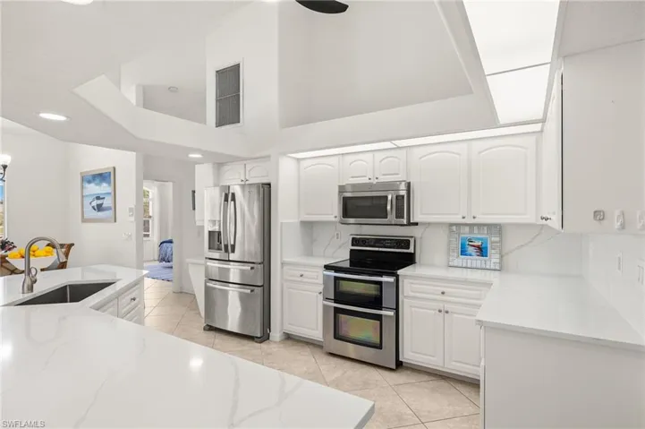 Kitchen with stainless steel appliances, light tile patterned floors, light stone countertops, white cabinetry, and backsplash