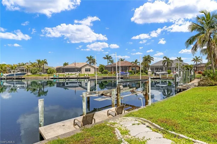 Dock with boat lift, a residential view, a water view, and a lawn