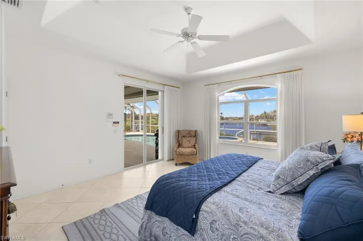 Bedroom featuring a water view, access to exterior, a tray ceiling, light tile patterned floors, and multiple windows