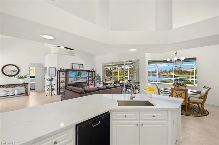 Kitchen with black dishwasher, light tile patterned floors, a towering ceiling, open floor plan, and light stone countertops