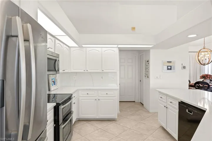 Kitchen with appliances with stainless steel finishes, a chandelier, white cabinetry, light tile patterned flooring, and recessed lighting
