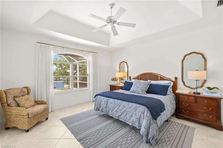 Bedroom with a tray ceiling, light tile patterned flooring, and ceiling fan