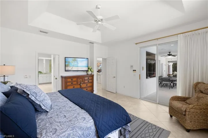 Bedroom featuring access to exterior, light tile patterned flooring, a ceiling fan, ensuite bathroom, and a tray ceiling
