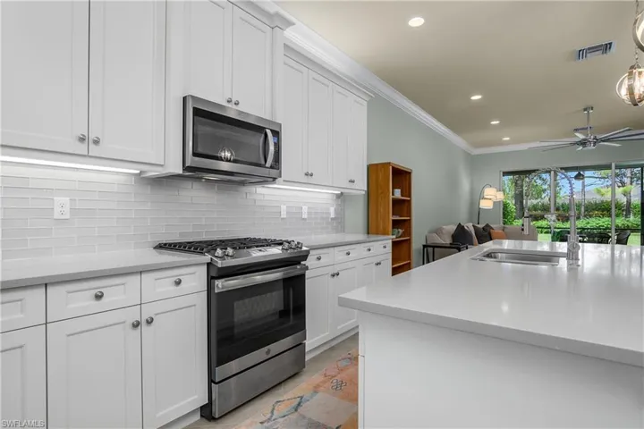 Kitchen with stainless steel appliances, decorative backsplash, white cabinetry, recessed lighting, and light stone counters