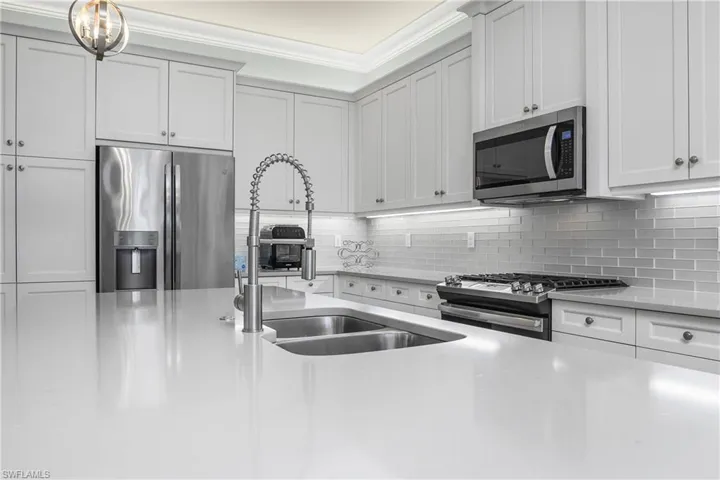 Kitchen featuring appliances with stainless steel finishes, white cabinets, backsplash, crown molding, and light stone countertops