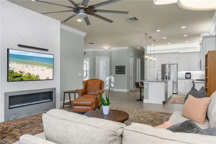 Living room with crown molding, light tile patterned flooring, recessed lighting, a glass covered fireplace, and ceiling fan