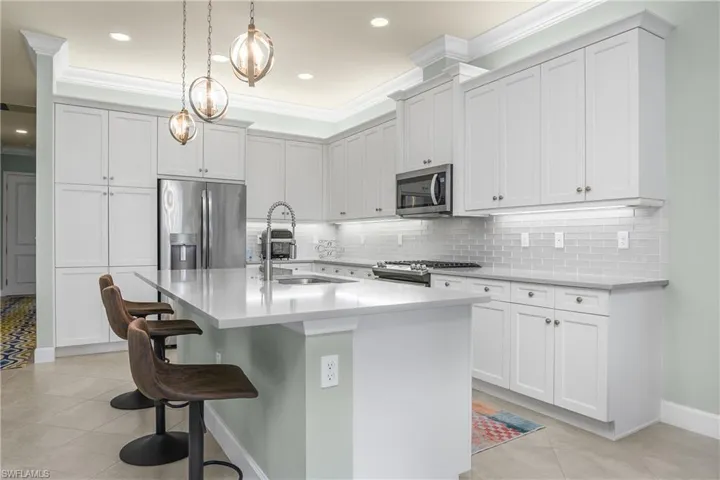 Kitchen featuring light tile patterned flooring, stainless steel appliances, a kitchen breakfast bar, an island with sink, and white cabinets