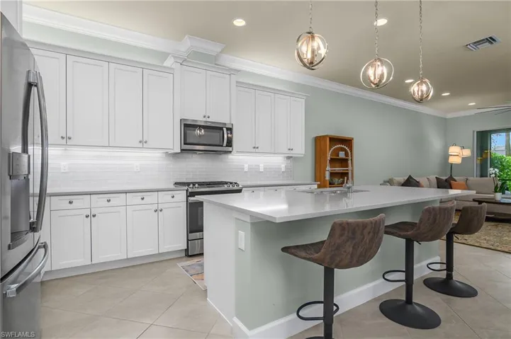 Kitchen featuring appliances with stainless steel finishes, crown molding, decorative backsplash, white cabinets, and a kitchen bar