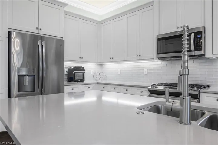 Kitchen with stainless steel appliances, tasteful backsplash, white cabinets, light stone countertops, and ornamental molding