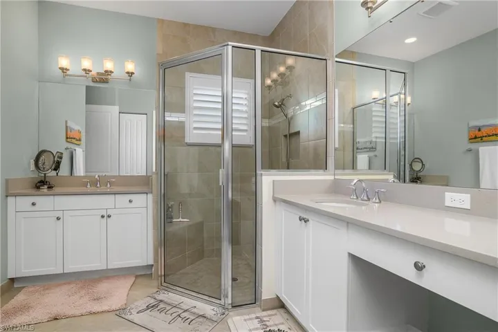 Primary bathroom featuring a shower stall, two vanities, and light tile patterned floors