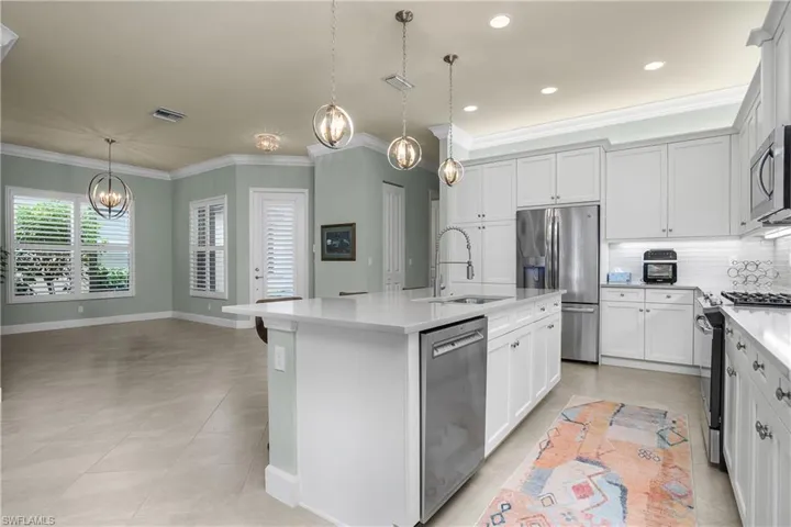Kitchen featuring decorative backsplash, appliances with stainless steel finishes, decorative light fixtures, a kitchen island with sink, and crown molding