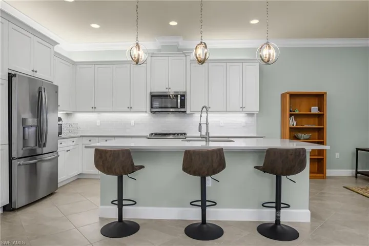Kitchen featuring stainless steel appliances, ornamental molding, backsplash, a kitchen breakfast bar, and a center island with sink