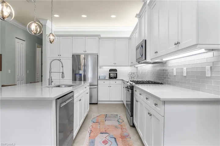 Kitchen featuring appliances with stainless steel finishes, a center island with sink, decorative light fixtures, light tile patterned floors, and white cabinets