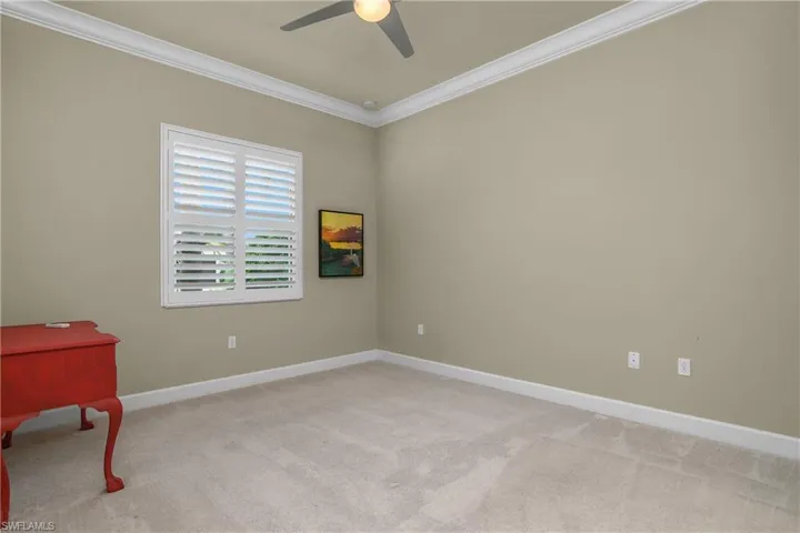 Spacious guest bedroom with lush carpet, plantation shutters, crown molding, and a ceiling fan.