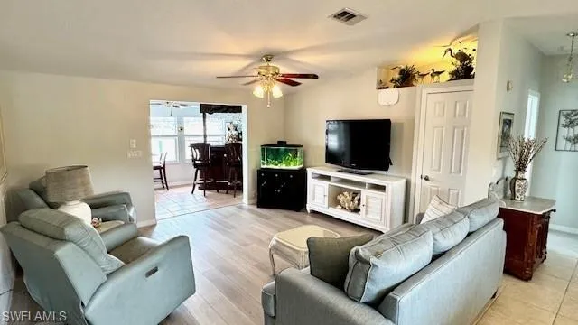 Living room featuring ceiling fan with notable chandelier and light wood-type flooring