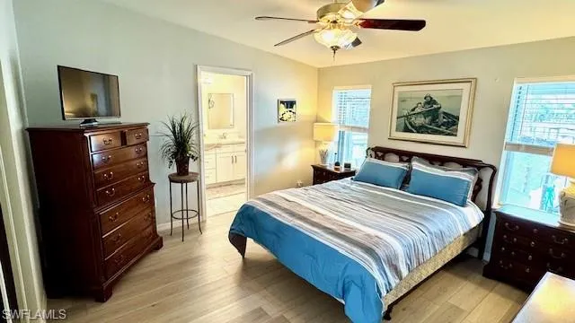 Bedroom with multiple windows, ceiling fan, light hardwood / wood-style floors, and connected bathroom