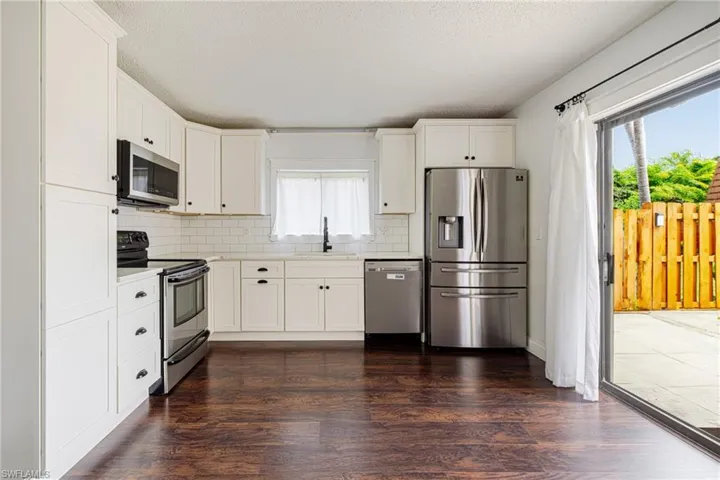Kitchen featuring white cabinetry, stainless steel appliances, dark wood-finish flooring, subway tile backsplash, and a sliding glass door to the patio