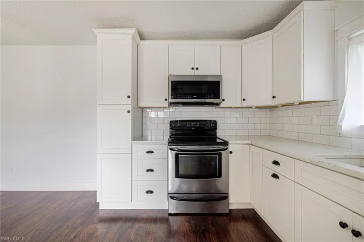 Modern kitchen featuring white shaker cabinetry, stainless steel appliances, a subway tile backsplash, light-toned countertops, and wood-finish flooring