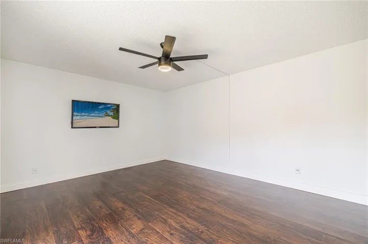 Spacious room featuring rich wood-finish flooring, white walls, and a textured ceiling
