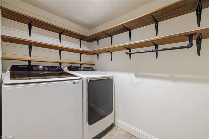 Utility area featuring substantial wood-finish shelving with black metal brackets, a black pipe hanging rod, and light wood-finish flooring