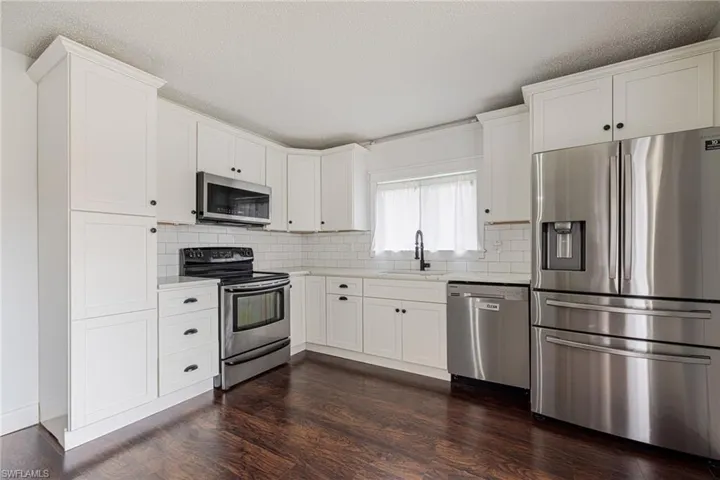 Kitchen featuring white shaker-style cabinetry, stainless steel appliances, dark wood-finish flooring, white subway tile backsplash, and light countertops
