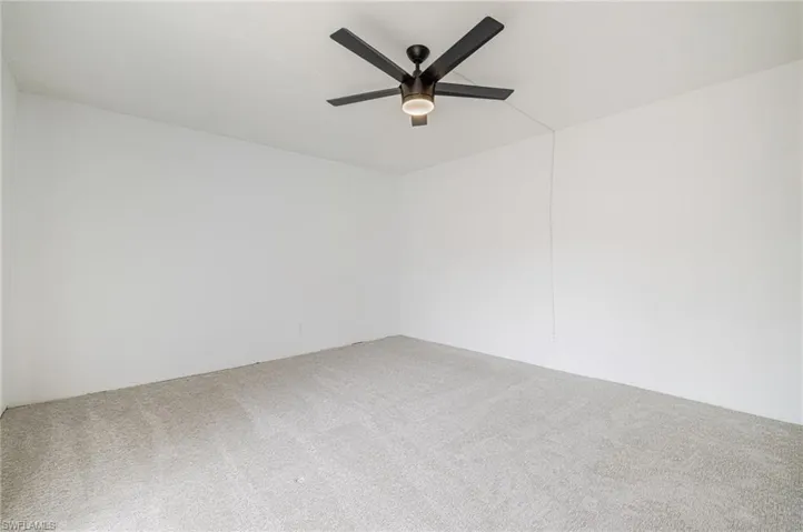 Spacious interior room featuring light-colored carpeting, white walls, and a contemporary ceiling fan with integrated lighting
