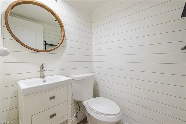 Bathroom featuring white shiplap walls, a white vanity with two drawers, a rectangular undermount sink with a brushed nickel faucet, a white toilet, and an oval mirror with a wood-finish frame