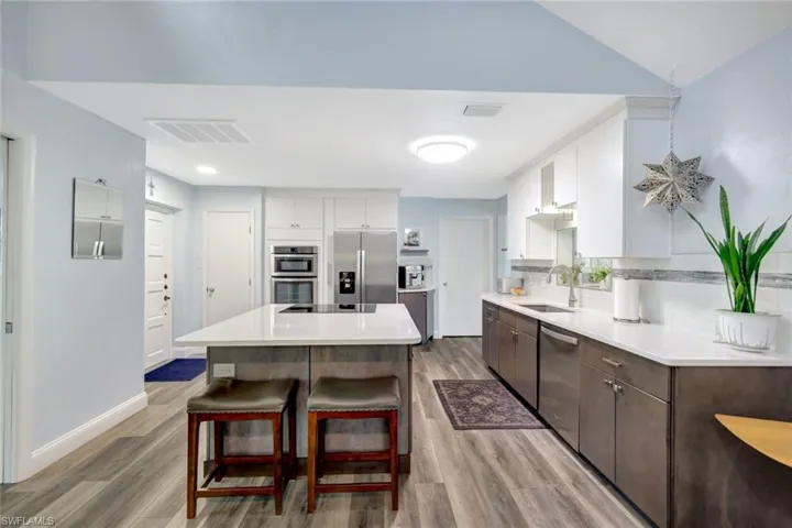 Kitchen featuring stainless steel appliances, wood-type flooring, white cabinetry, and sink