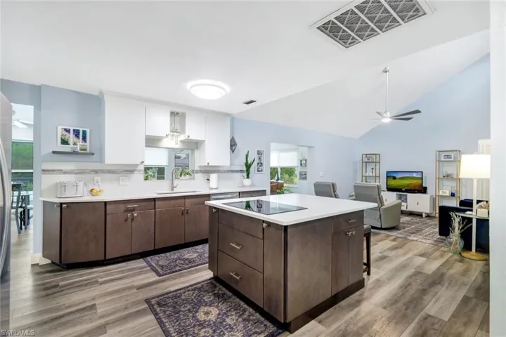 Kitchen with vaulted ceiling, sink, dark brown cabinets, white cabinetry, and light wood-type flooring