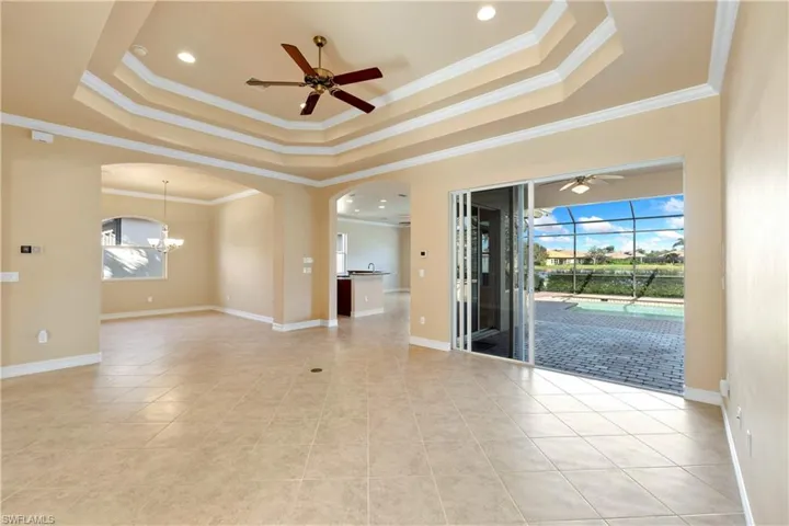 Tiled empty room with ornamental molding, ceiling fan with notable chandelier, and a raised ceiling
