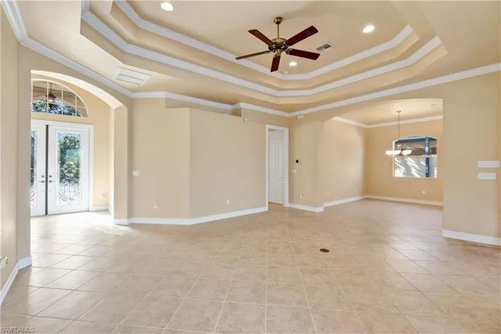 Tiled empty room with crown molding, ceiling fan with notable chandelier, and a raised ceiling