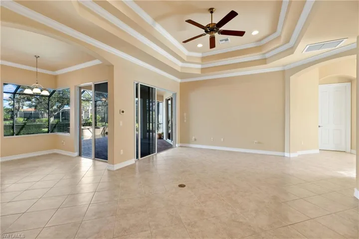 Unfurnished room featuring light tile patterned flooring, ornamental molding, a tray ceiling, and ceiling fan with notable chandelier