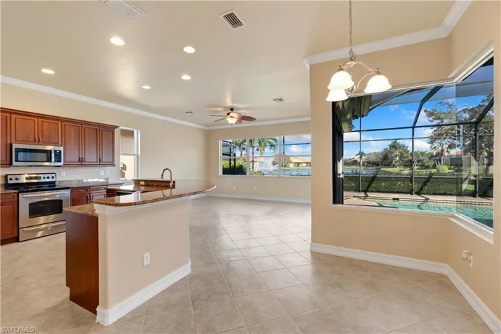 Kitchen featuring stone countertops, hanging light fixtures, stainless steel appliances, ornamental molding, and ceiling fan with notable chandelier